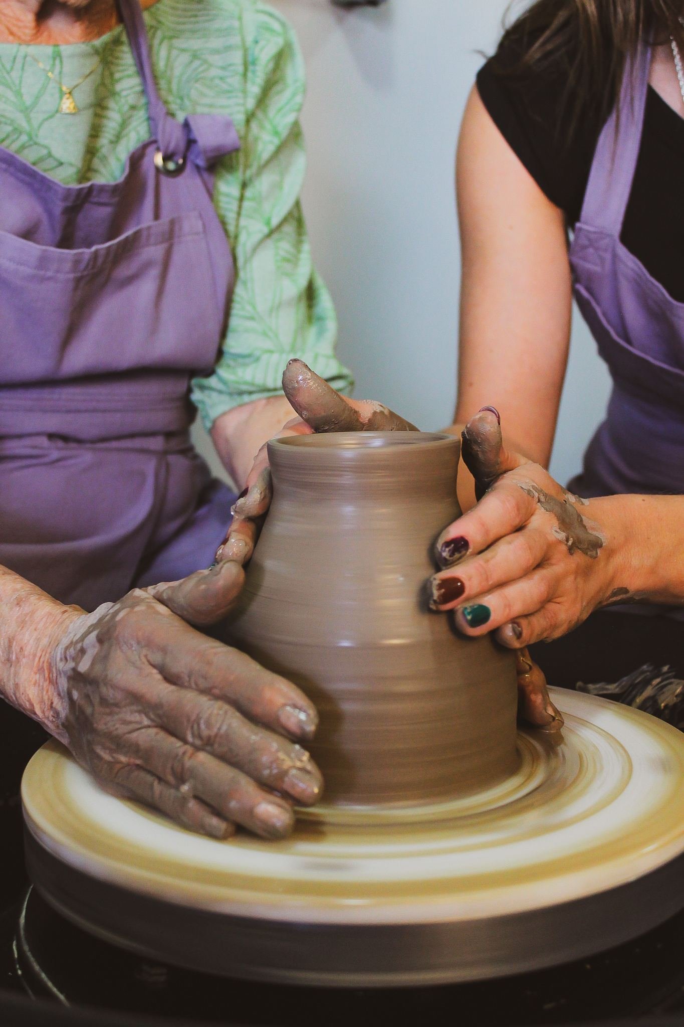 Várias mãos modelando juntas um vaso de argila no torno